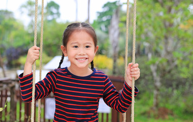 Close up happy little Asian child girl play and sitting on the swing in the nature park.