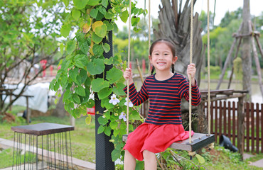 Portrait of smiling little Asian child girl play and sitting on the swing in the nature park.