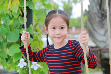 Close up happy little Asian child girl play and sitting on the swing in the nature park.