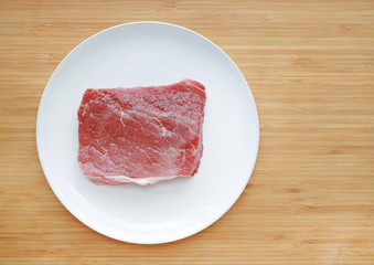 Raw beef meat on white plate against wooden backgroundwith copy space. Top view.