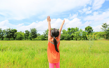 Rear view of little Asian child girl stretch arms and relaxed at the young green paddy fields