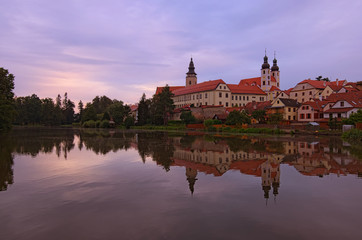 Fototapeta na wymiar Panoramic view of Telc castle, pond with park, Name of Jesus Church and tower of the Church of St. Jakub. Buildings are reflected in the water. Early morning landscape. A UNESCO World Heritage Site