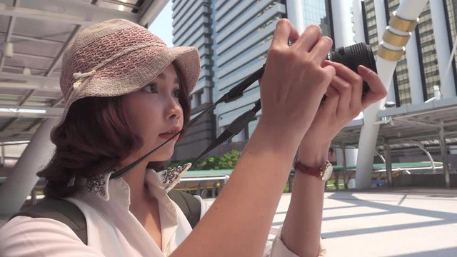 Slow motion - Cheerful Traveler backpacker Asian woman using camera to make photo while travel at downtown in Bangkok, Thailand. Woman tourist journey on holidays concept.