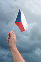 Hand holding Czech Republic flag high in the air, with a stormy, cloudy sky