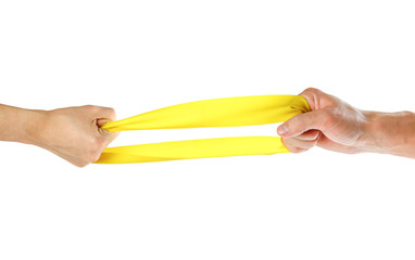 The hands pull yellow athletic elastic band in different directions. Close up. Isolated on white background