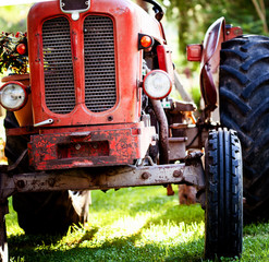 Fototapeta premium Croppped photo of old vintage red tractor standing on a farm field at sunset.