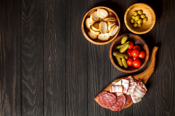 Ingredients for making tapas or bruschetta. Crusty bread, ham ,  tomatoes, olives on plates over dark texture background. Top view