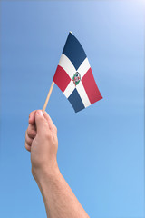 Hand holding Dominican Republic flag high in the air, with a clear blue sky