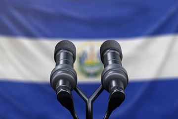 Podium lectern with two microphones and El Salvador flag in background