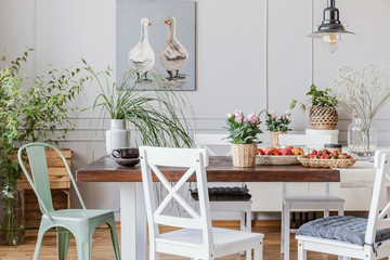 Rustic dining room with long table and white chairs and oil painting on the grey wall, real photo