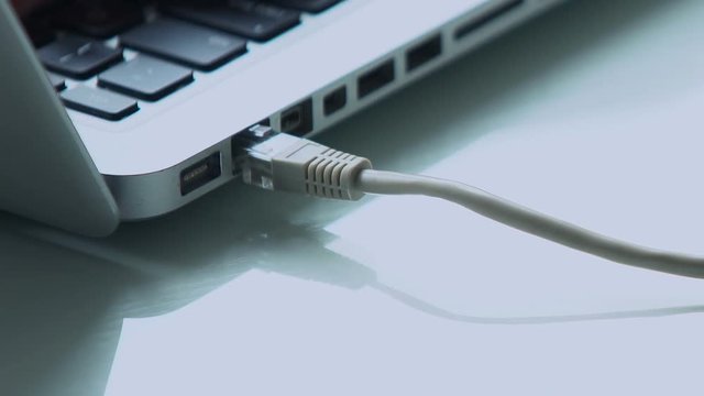 Female fingers plugging in ethernet cable into laptop port, network connection