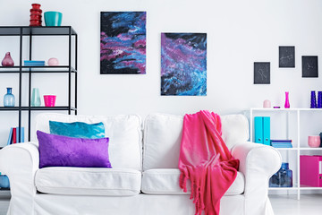 Closeup of white comfortable couch with pink blanket and purple and blue pillows in modern living...