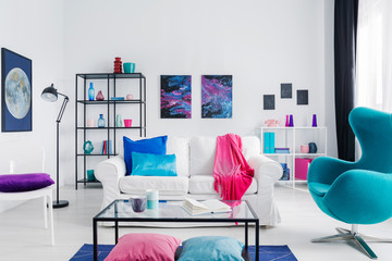 Eclectic living room with blue egg chair, metal coffee table and white couch with colorful pillows, real photo with copy space