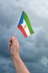 Hand holding Equatorial Guinea flag high in the air, with a stormy, cloudy sky