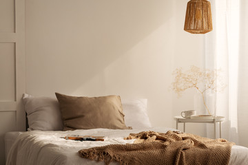 Closeup of bed with beige blanket and linen pillow in minimal bedroom interior, real photo with copy space on the empty wall