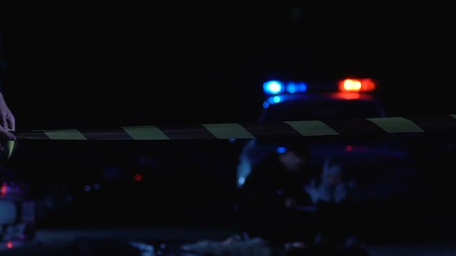 Police officer rolling tape on crime scene, protecting evidence from onlookers
