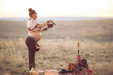 concept. Woman playing a Tibetan bowl. Pregnant woman doing yoga in the field at sunset.
