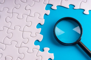 White jigsaw puzzle, Magnifier and missing pieces with selective focus and crop fragment. Business and education concept