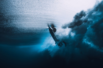 Surfer with surfboard dive underwater with under ocean wave.