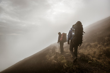 Hikers with backpacks on a misty mountain trail.
