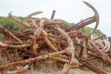 Stored old rusty ship anchors in rows in front of a Mediterranean landscape in Spain