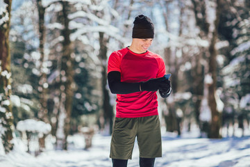 Young Man Taking Break from Jogging in the Forrest using Smart Phone