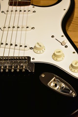 Black and white electric guitar closeup. Body details: Bridge, strings, jack, single coil pickups, knobs, switch and pickguard.