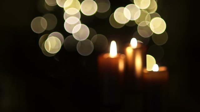 Close up of three burning candles with blurred Christmas light background. Dynamic focus, celebration of Christmas, All Saints Day, Halloween