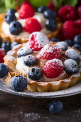  Dessert tarts with raspberries and blueberries on a wooden table.