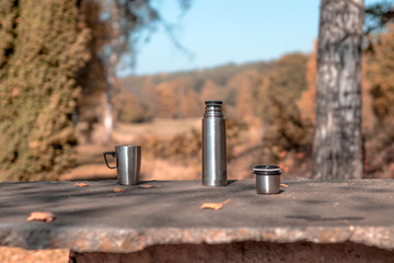 A cup of tee standing on a outdoor desk in a beautidul autumn scenery. coffee, tee, fall, landscape, cup, outdoor drink;