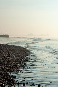 Skeletal West Pier appearing through sea mist at low tide on Brighton beach