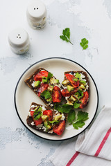 Avocados, cherry tomatoes and feta cheese sandwiches with balsamic sauce and cilantro on old olive board. Top view.
