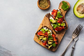 Avocados, cherry tomatoes and feta cheese sandwiches with balsamic sauce and cilantro on old olive board. Top view.