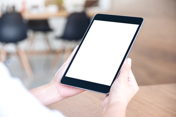 Mockup image of hands holding and using black tablet pc with blank white desktop screen while sitting in office