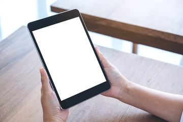 Mockup image of hands holding and using black tablet pc with blank white desktop screen while...