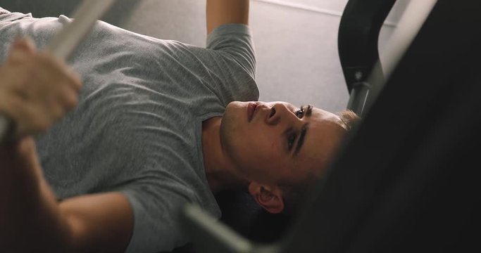 Young beginner man exercising with barbell in gym making bench press