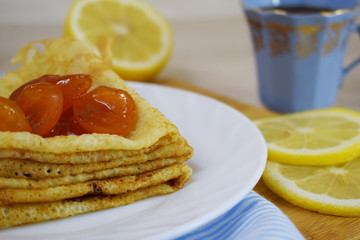 Delicious hot pancakes with apricot jam on a white plate and tea with lemon.