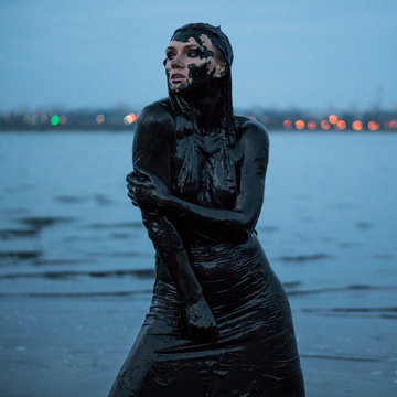 Portrait of an Adorable Caucasian Girl posing Smeared with a Healthy Black Mud in old Firth