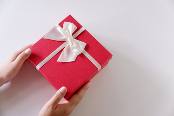 Close-up women hands sending red gift box with white ribbon on white background.