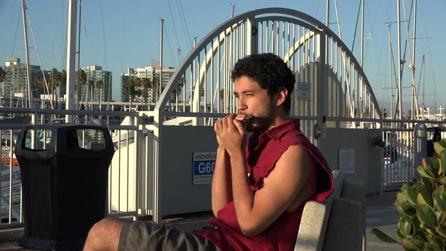 Young man playing the harmonica on the docks and laughing
