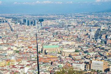 Bright skyline view of Naples, Italy with Mount Vesuvius standing above a cityscape dominated by an old church in the foreground