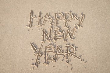 Happy New Year message handwritten in smooth sand under bright tropical sunlight
