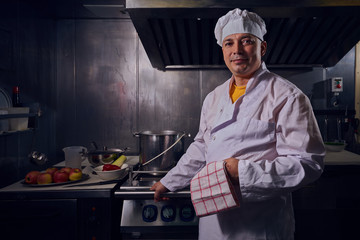 Chef cook in a white apron and cooks hat on a kitchen.