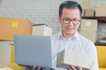 Young Asian businessman in casual shirt looking notebook at hand,  working in simple house office look like doing startup business. Concept for online marketing, SME and home base workplace