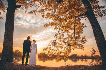 Wedding photo, bride and groom looking together at autumn sunset
