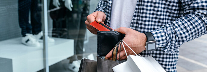 Young man with shopping bags taking out credit card from wallet
