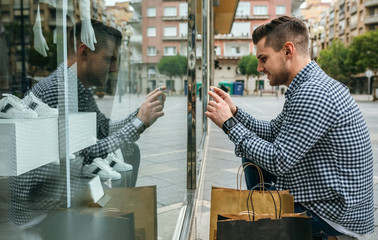 Young man taking a photo of a mannequin from a shop window of a fashion store