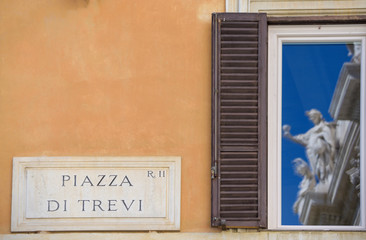 Fototapeta na wymiar Trevi Fountain, tourist attraction in Rome, Italy. The famous fountain of the sweet life is reflected in the windows next to the street sign of Piazza Trevi