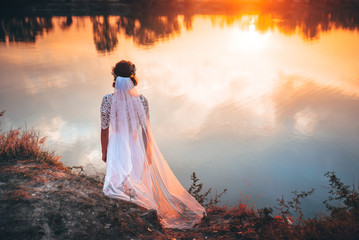 Bride by lake with autumn orange sunset. Wedding photo, edit space