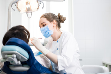 Dentist in uniform treats the patient's teeth in the white office